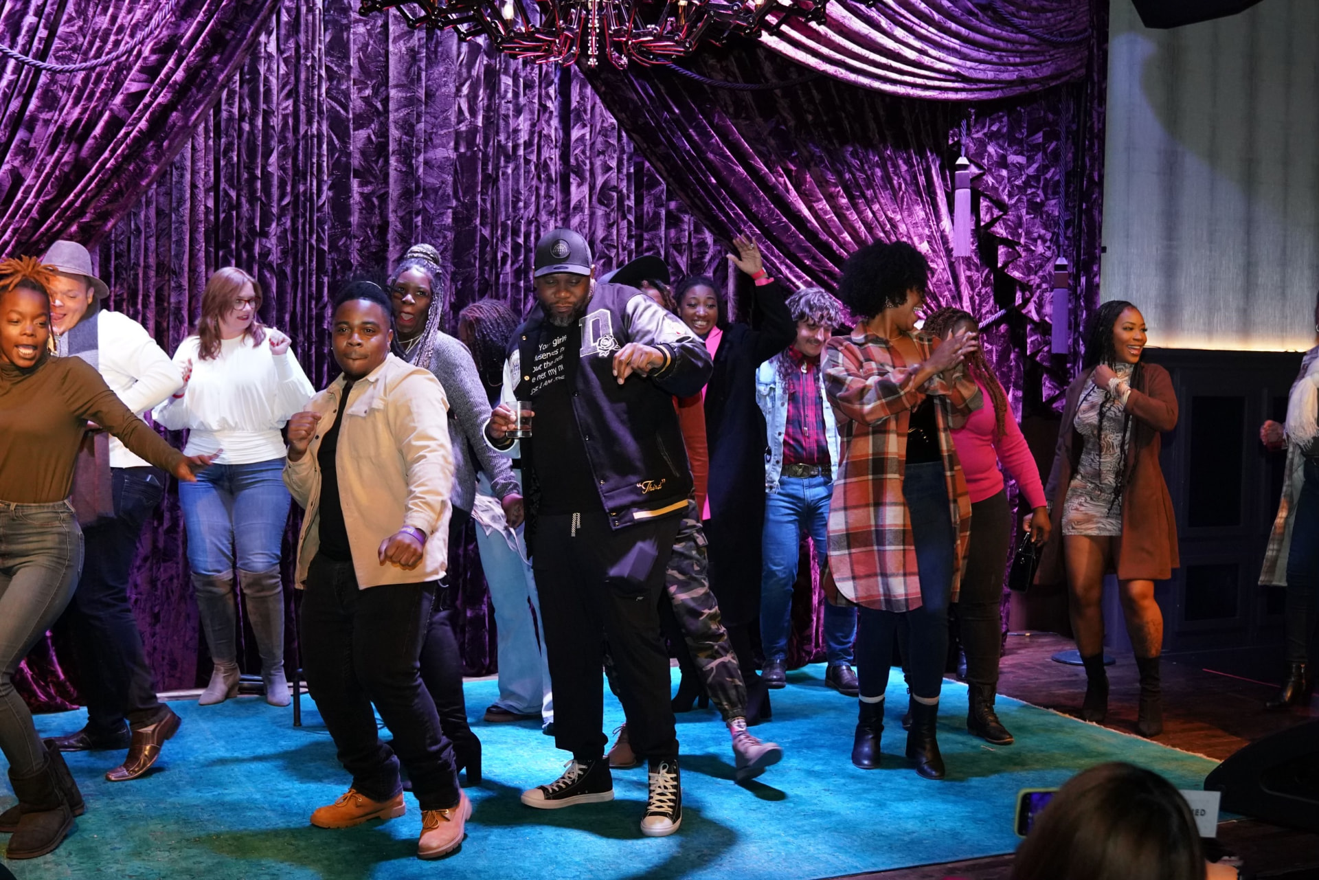 Audience dancing on stage in front of purple velvet curtains